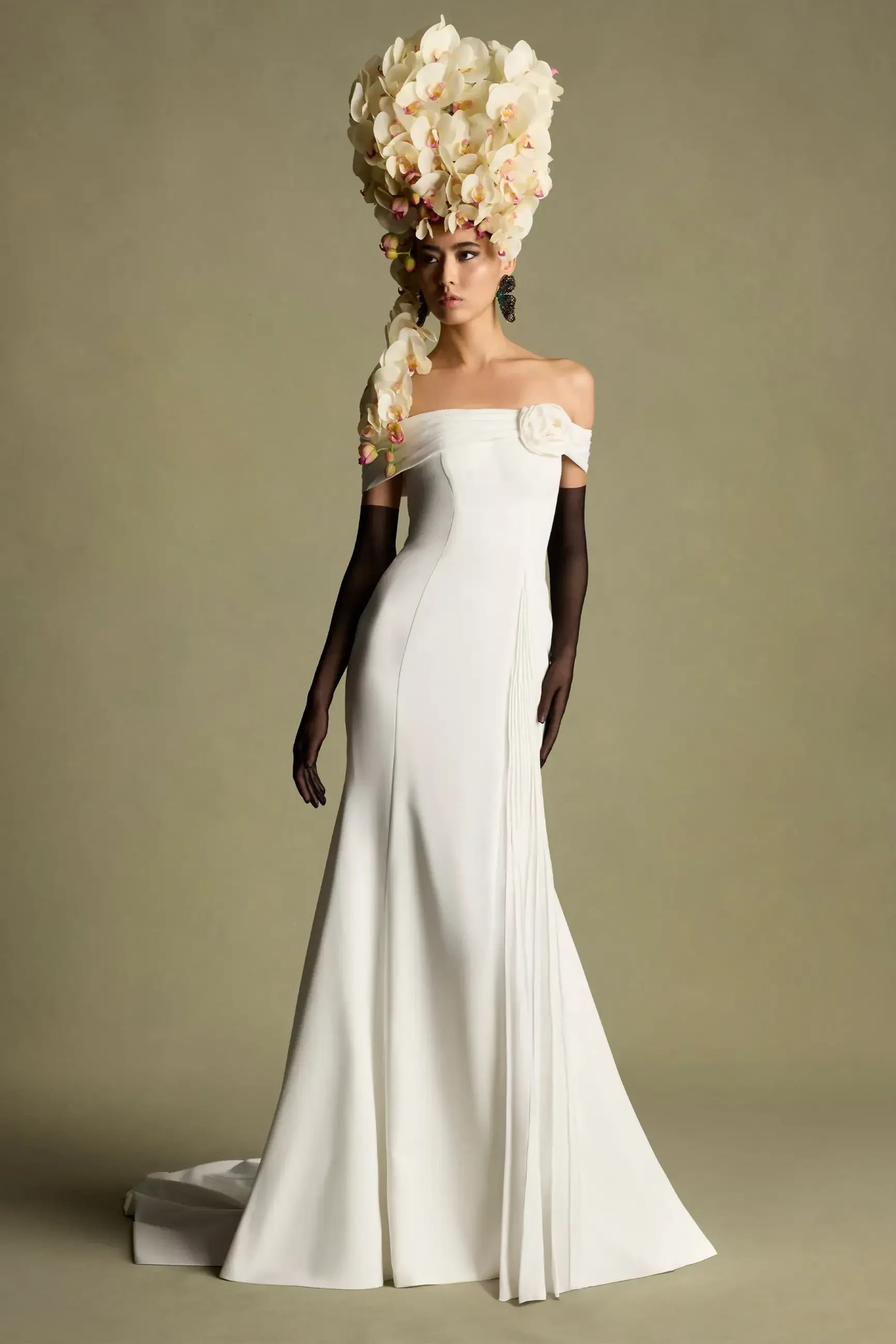 A model wearing an elegant off-shoulder white gown with a dramatic floral headpiece.