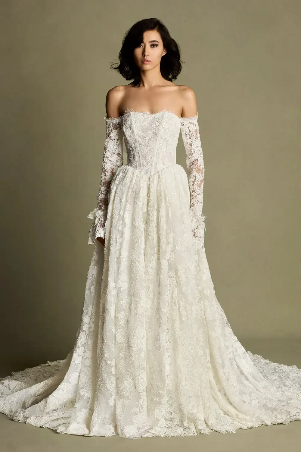 A model wearing a strapless, off-the-shoulder wedding gown with long lace sleeves and a full skirt.