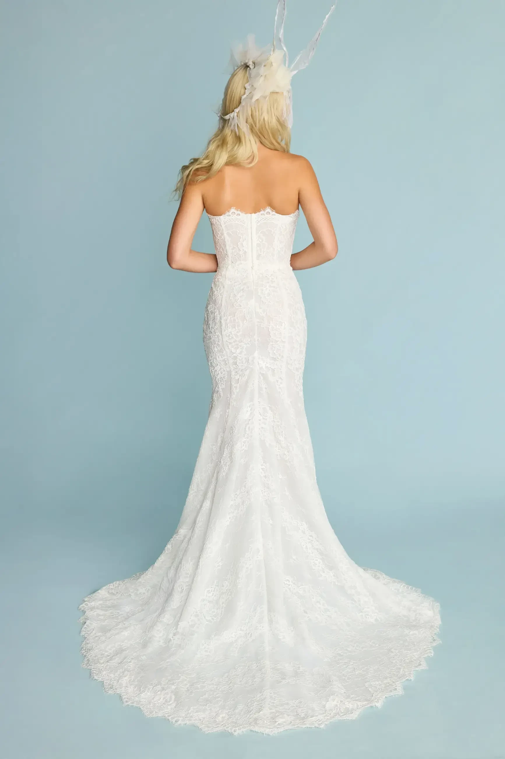 A back view of a woman wearing a fitted white wedding dress with a long train.